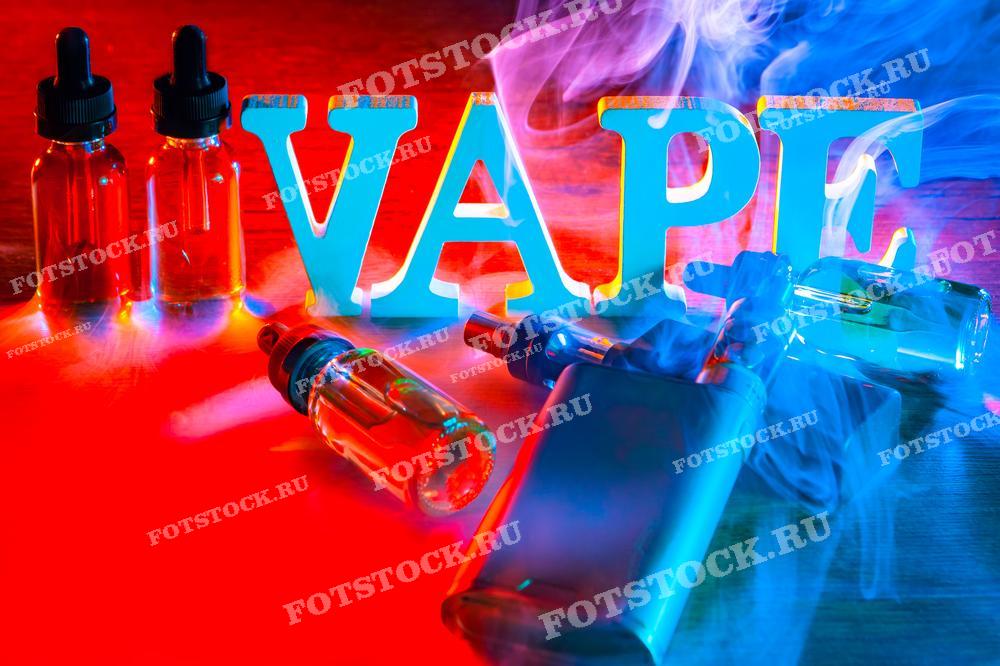 На фотографии изображены буквы, составляющие слово "VAPE", окруженные разноцветным дымом. Рядом находятся бутылочки с жидкостью для вейпа и устройства для вейпинга. Яркие цвета и дым создают динамичное и привлекающее внимание изображение.